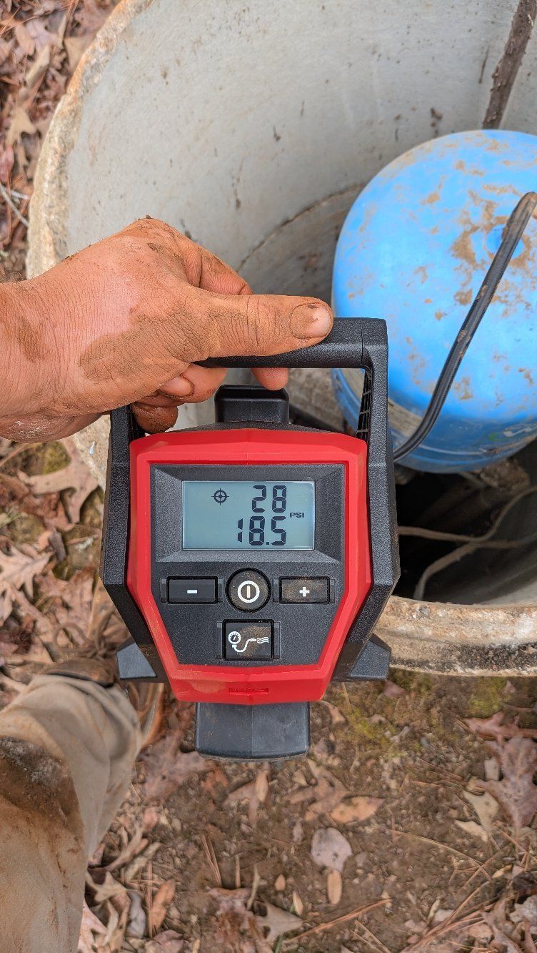 Hand holding a red digital meter reading 85 beside a blue tank outdoors