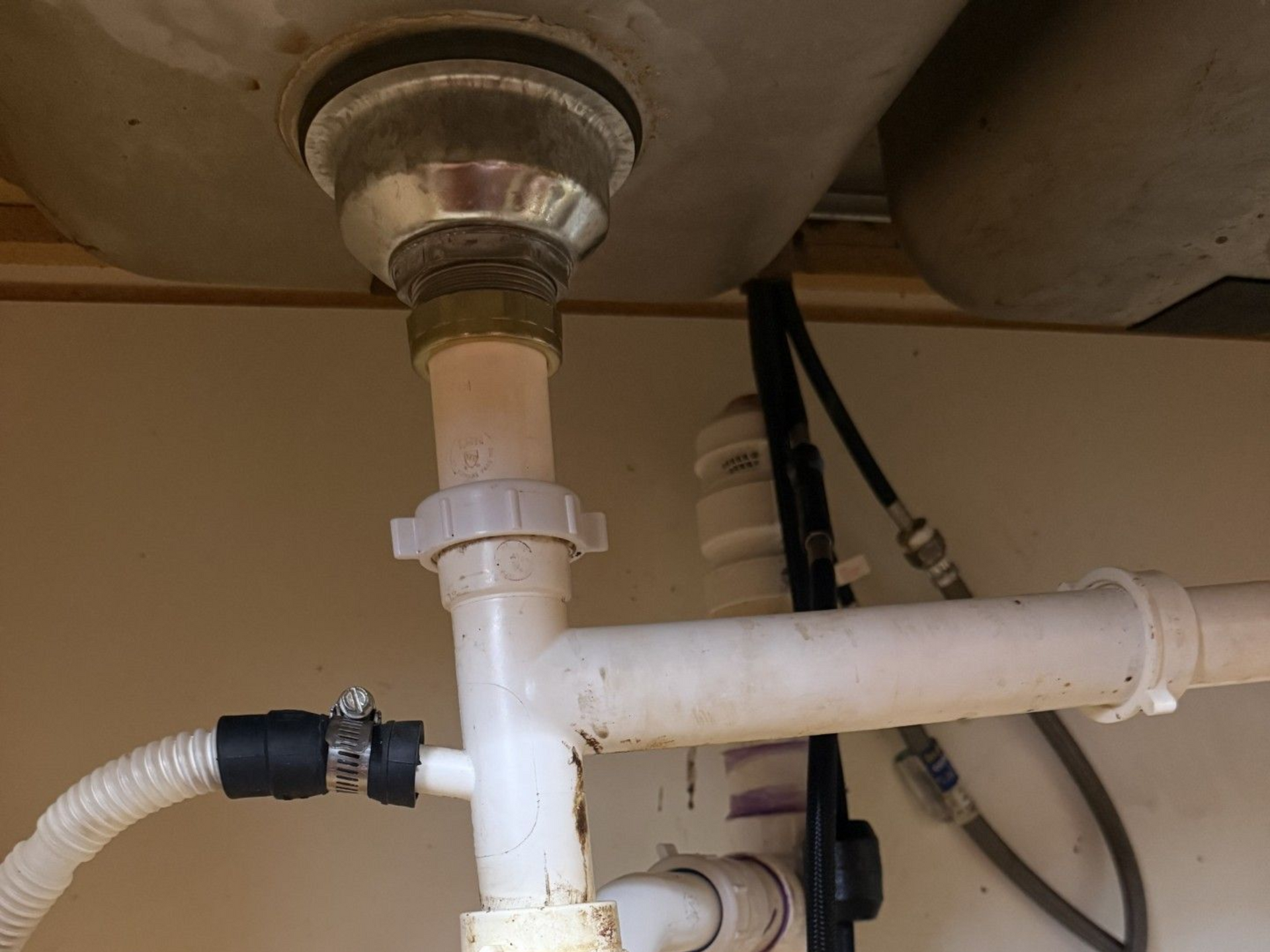 Under-sink plumbing with white PVC drain pipes and a black hose connection under a sink.