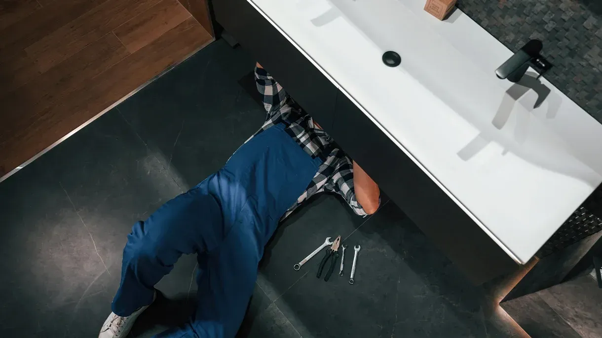 A plumber is laying on the floor under a sink in a bathroom.