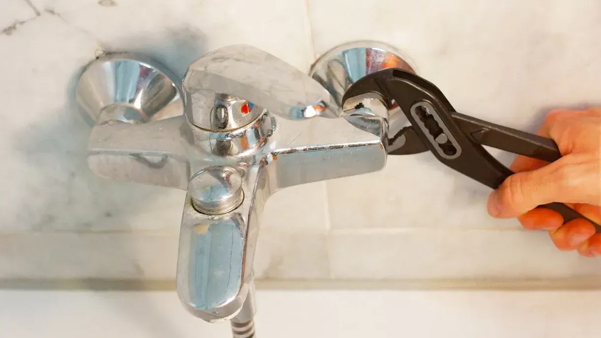 A person is fixing a faucet with a wrench.
