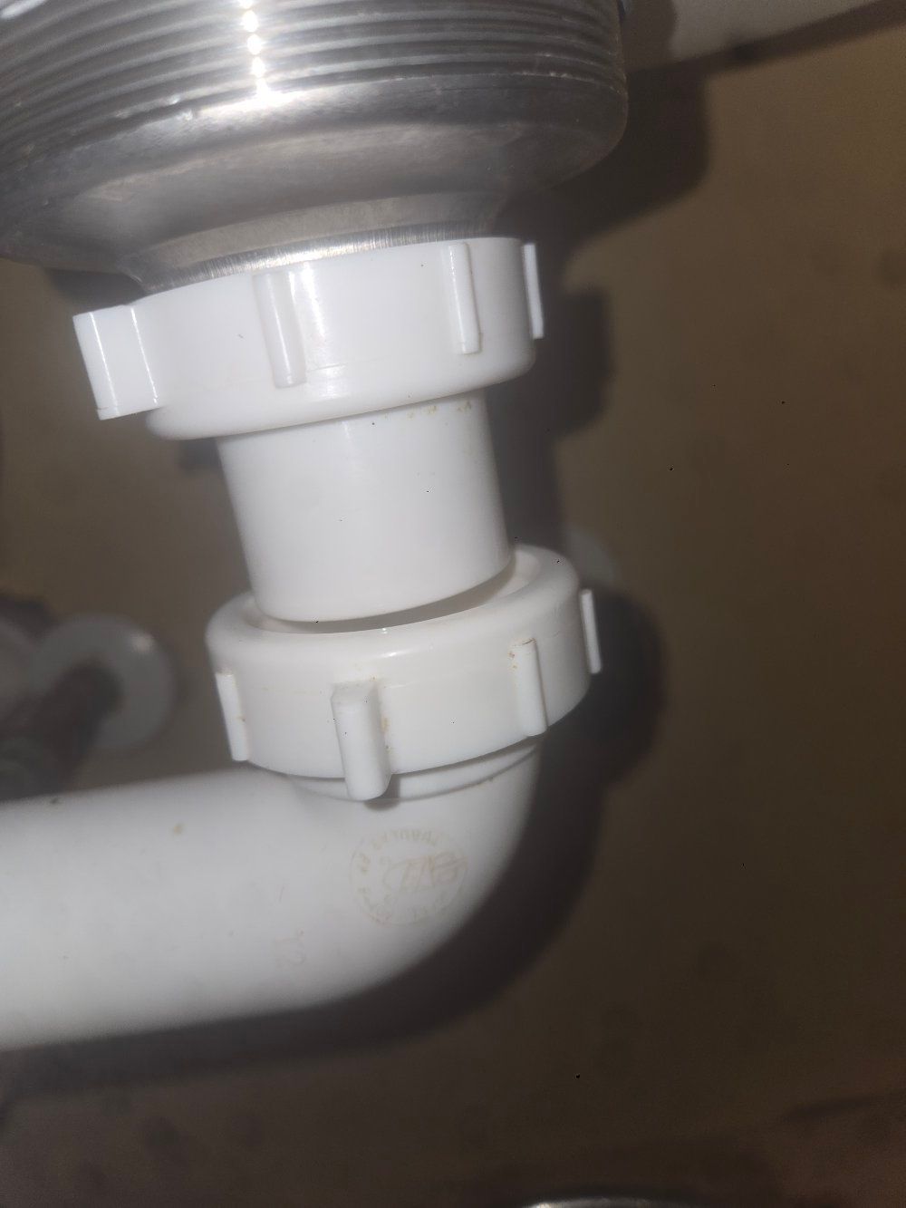 Close-up of a white plastic plumbing connector under a sink with a gray pipe above and a white drain pipe below