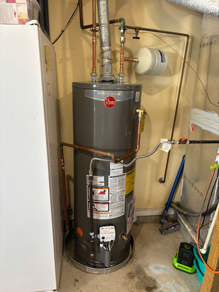 Water heater in a utility closet with pipes, a gas line, and nearby cleaning supplies.