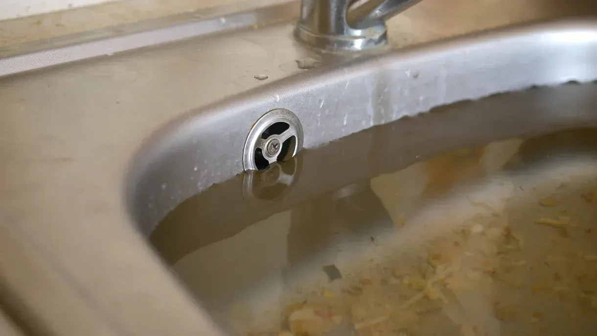 A close up of a dirty kitchen sink with water coming out of the drain.