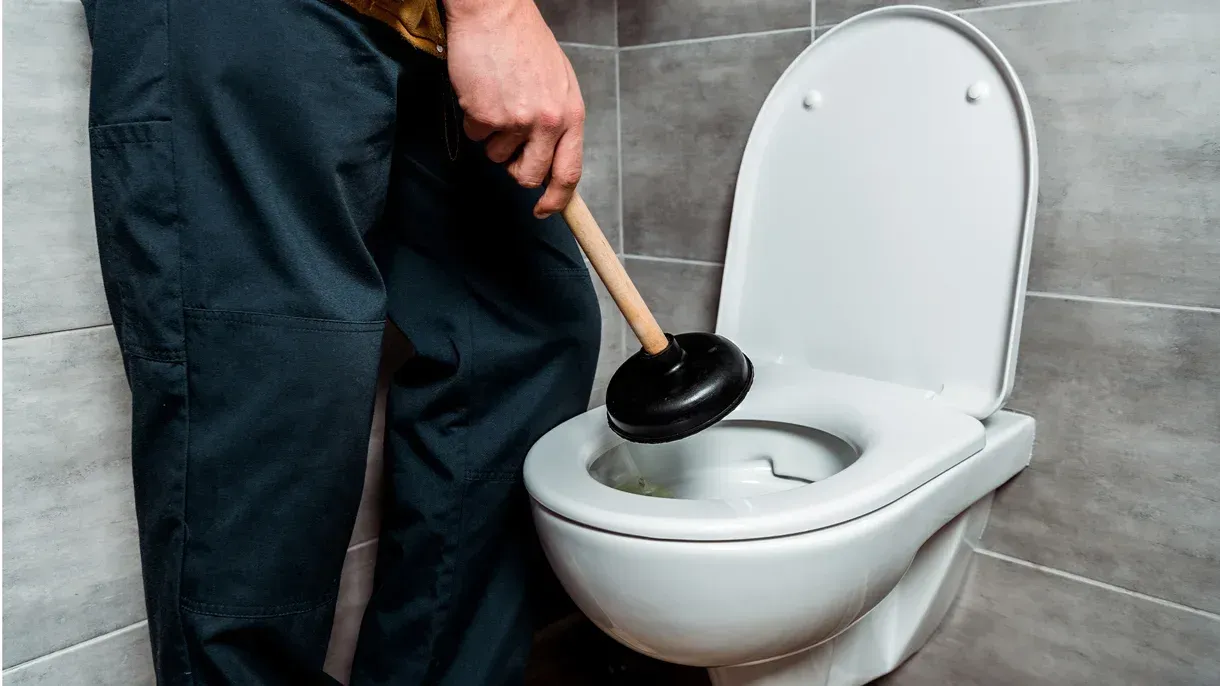 A man is using a plunger to unblock a toilet.