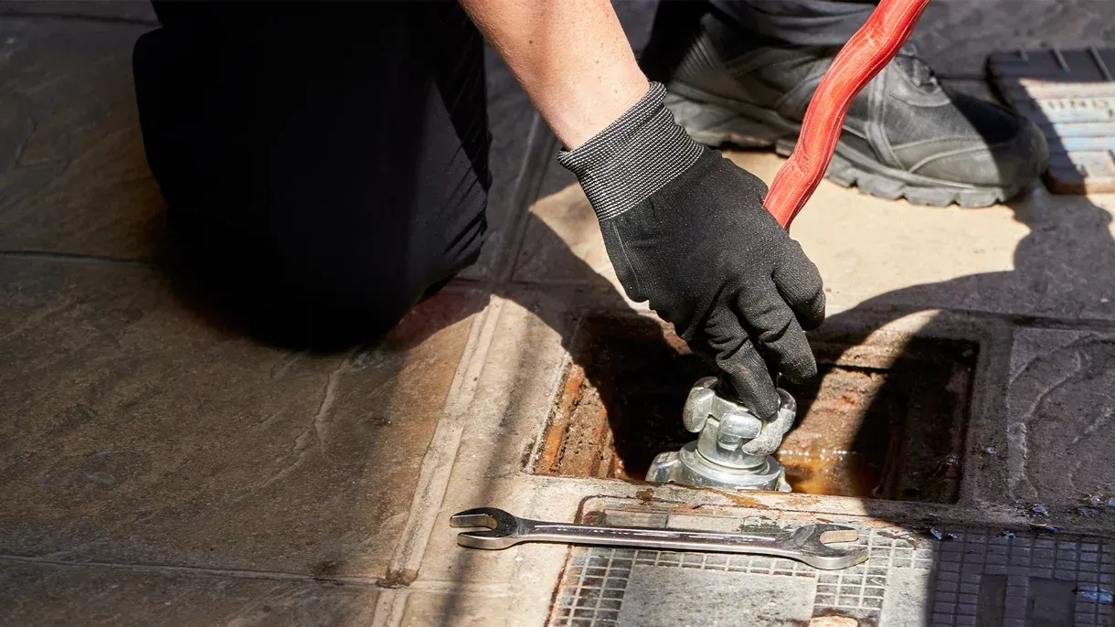 A man is kneeling down to fix a drain with a wrench.