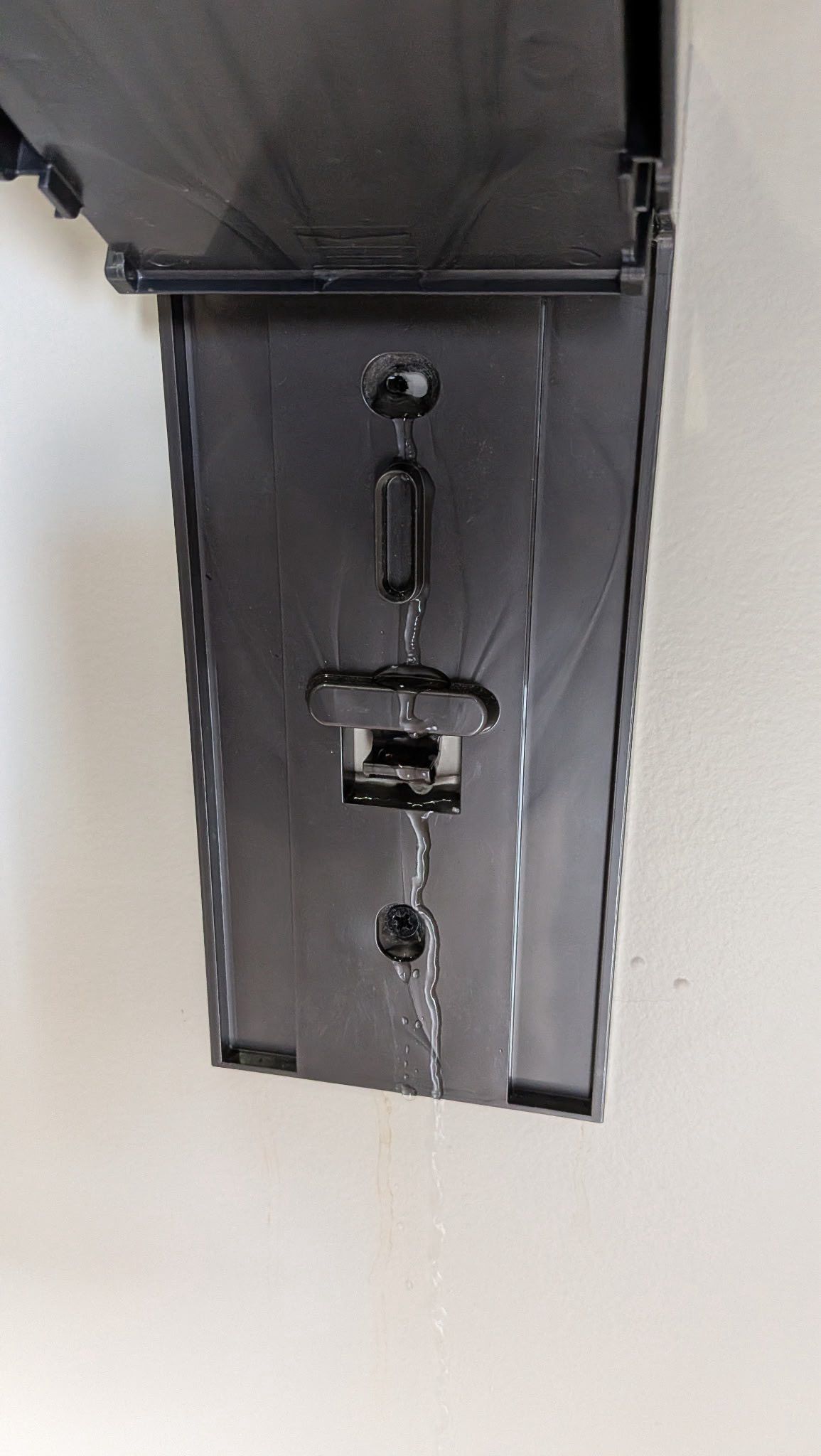 Dark metal wall-mounted bracket with a hanging latch on a light wall.