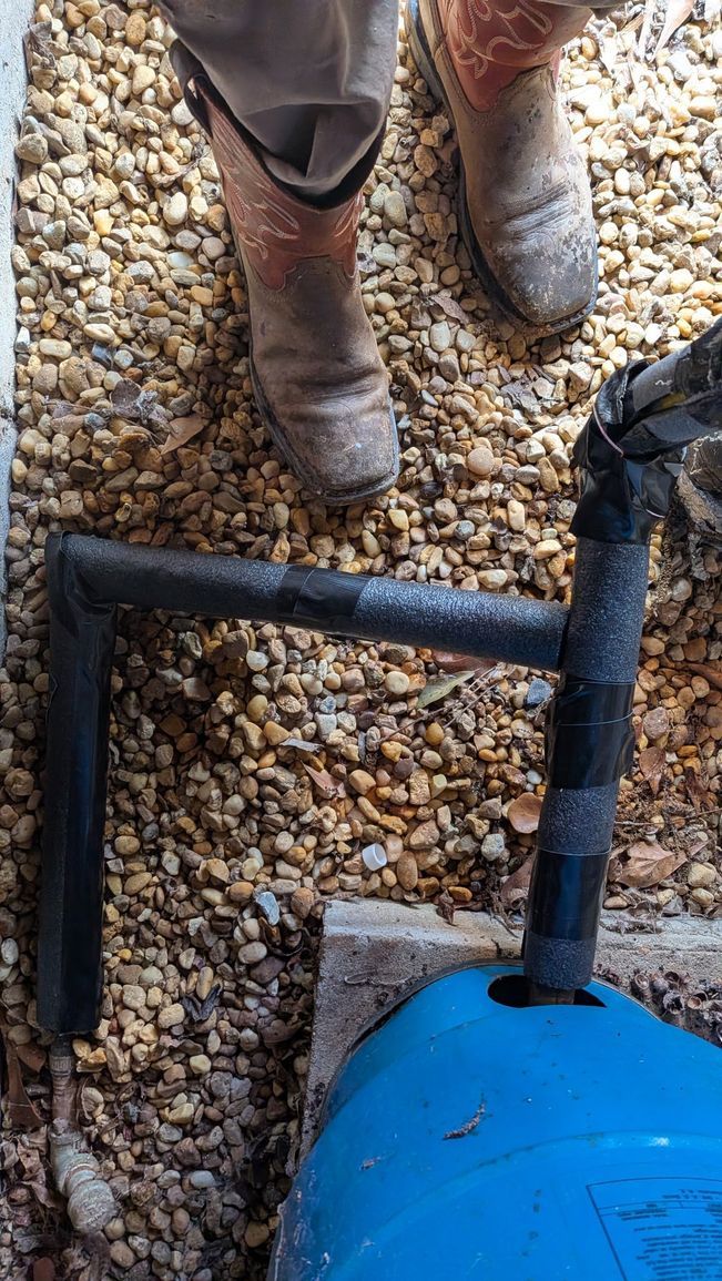 Blue industrial tank with black pipe on gravel beside a person's boots
