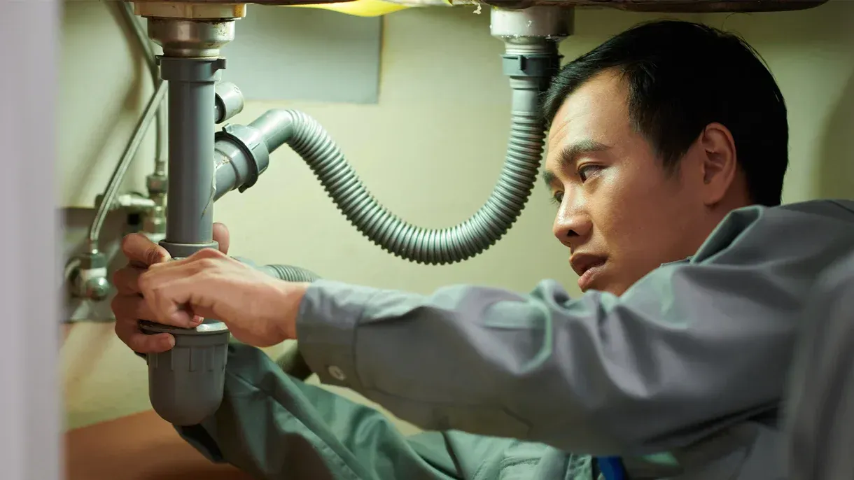 A man is fixing a sink pipe with a wrench.