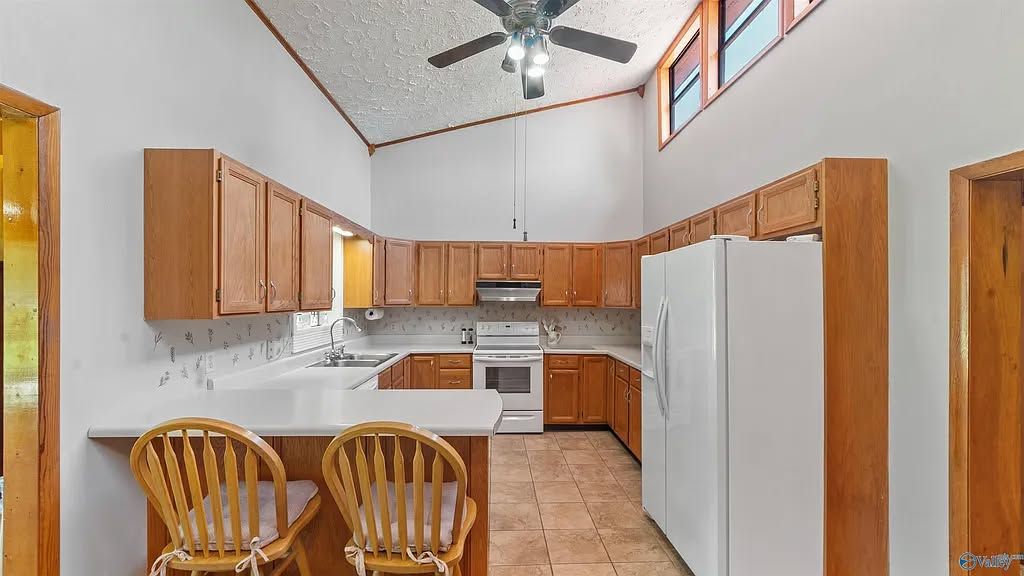 Bright kitchen with wood cabinets, white appliances, tile floor, and two wooden chairs by the counter.