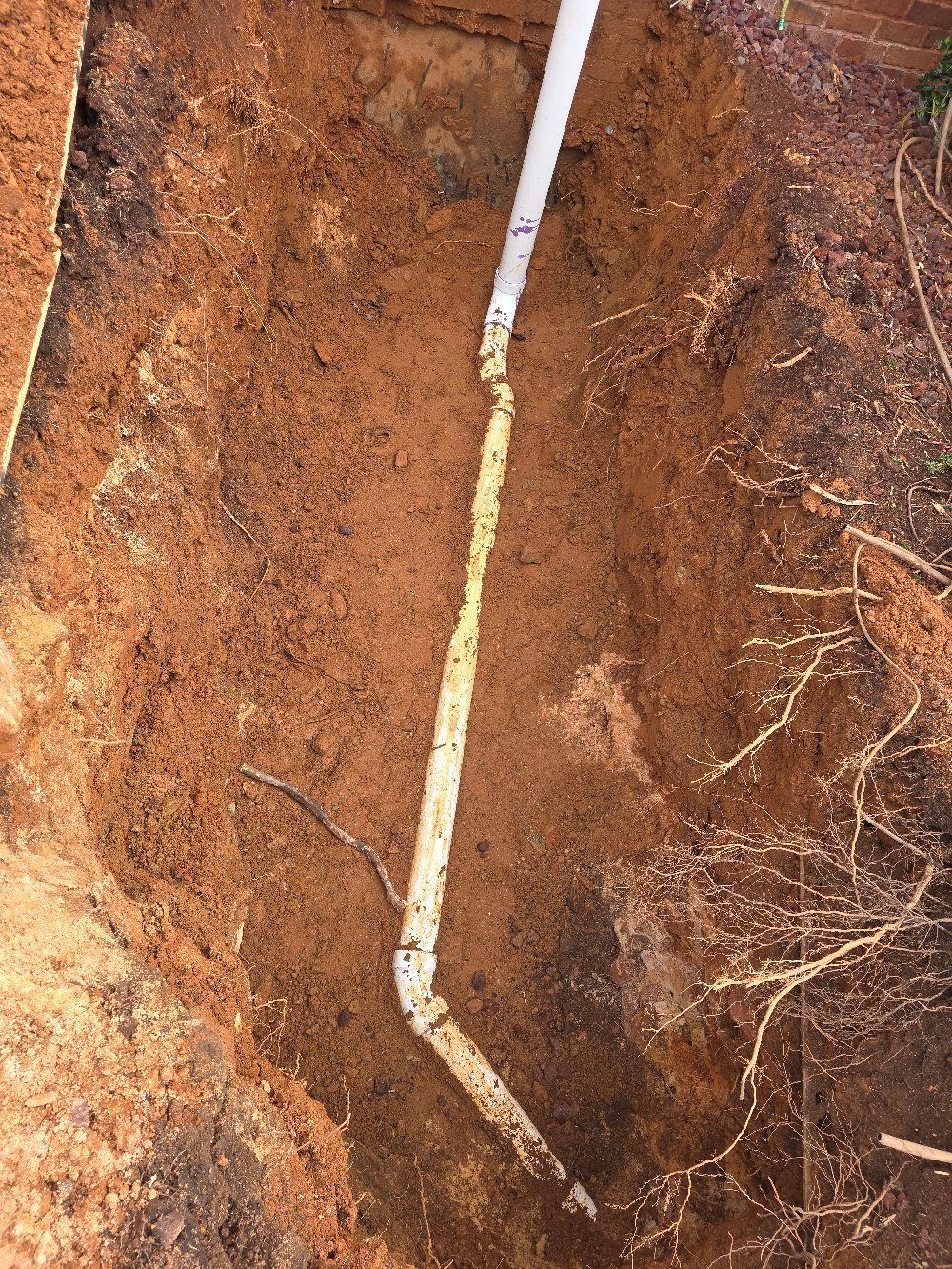 White drainpipe in a muddy trench with exposed soil and roots