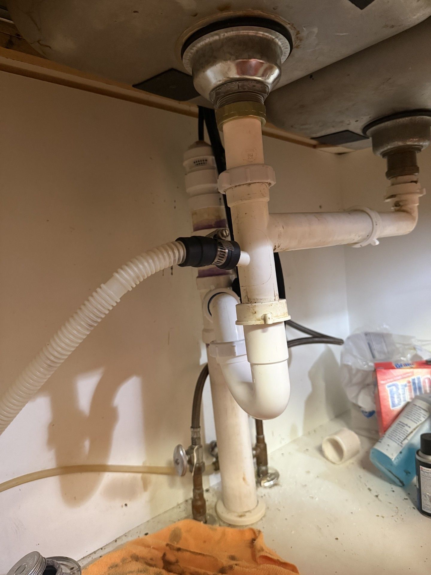 Under-sink plumbing with white pipes and flexible drain hose inside a cabinet