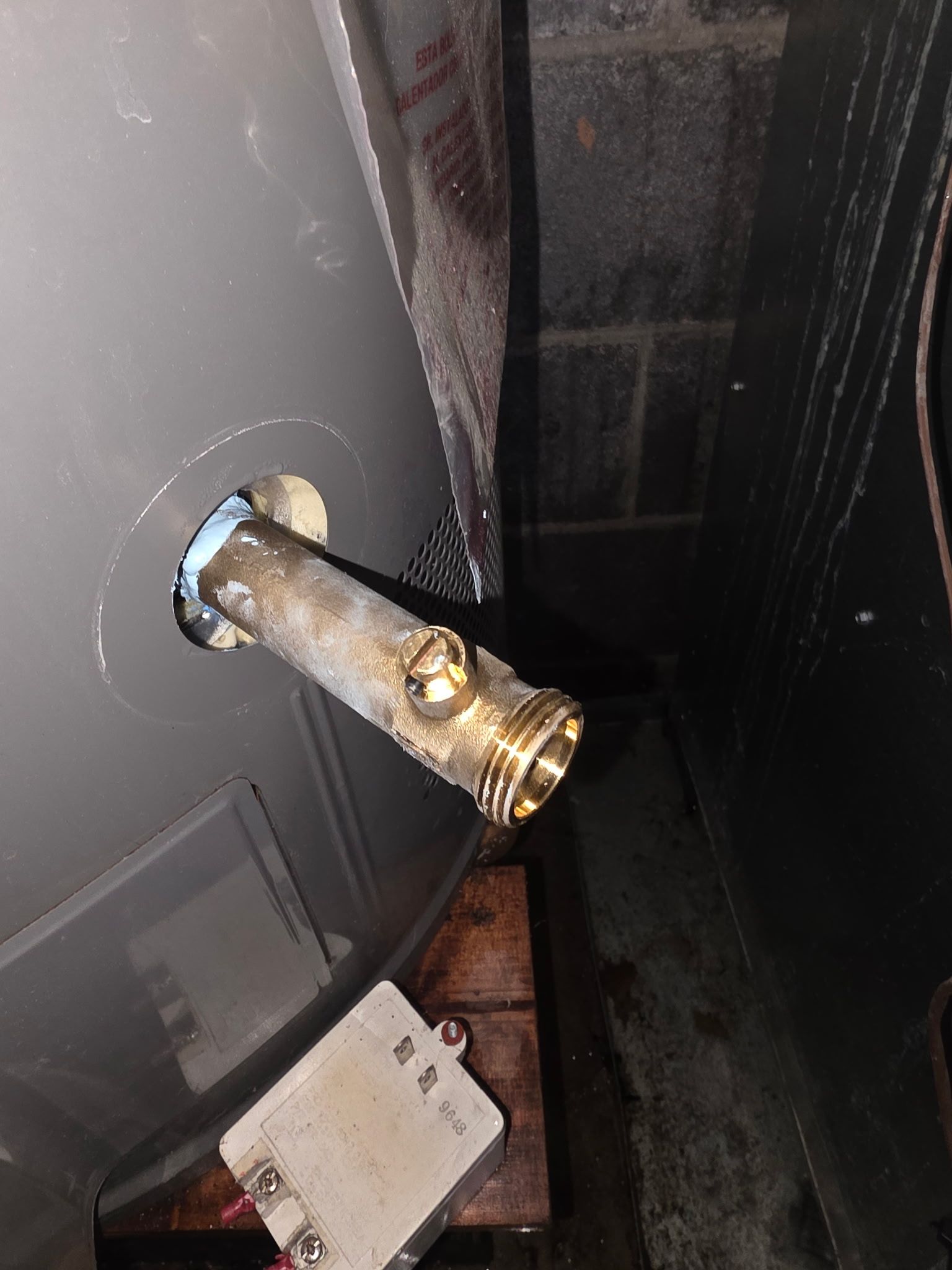 Close-up of a brass pipe valve protruding from a dark gray wall beside a black appliance.