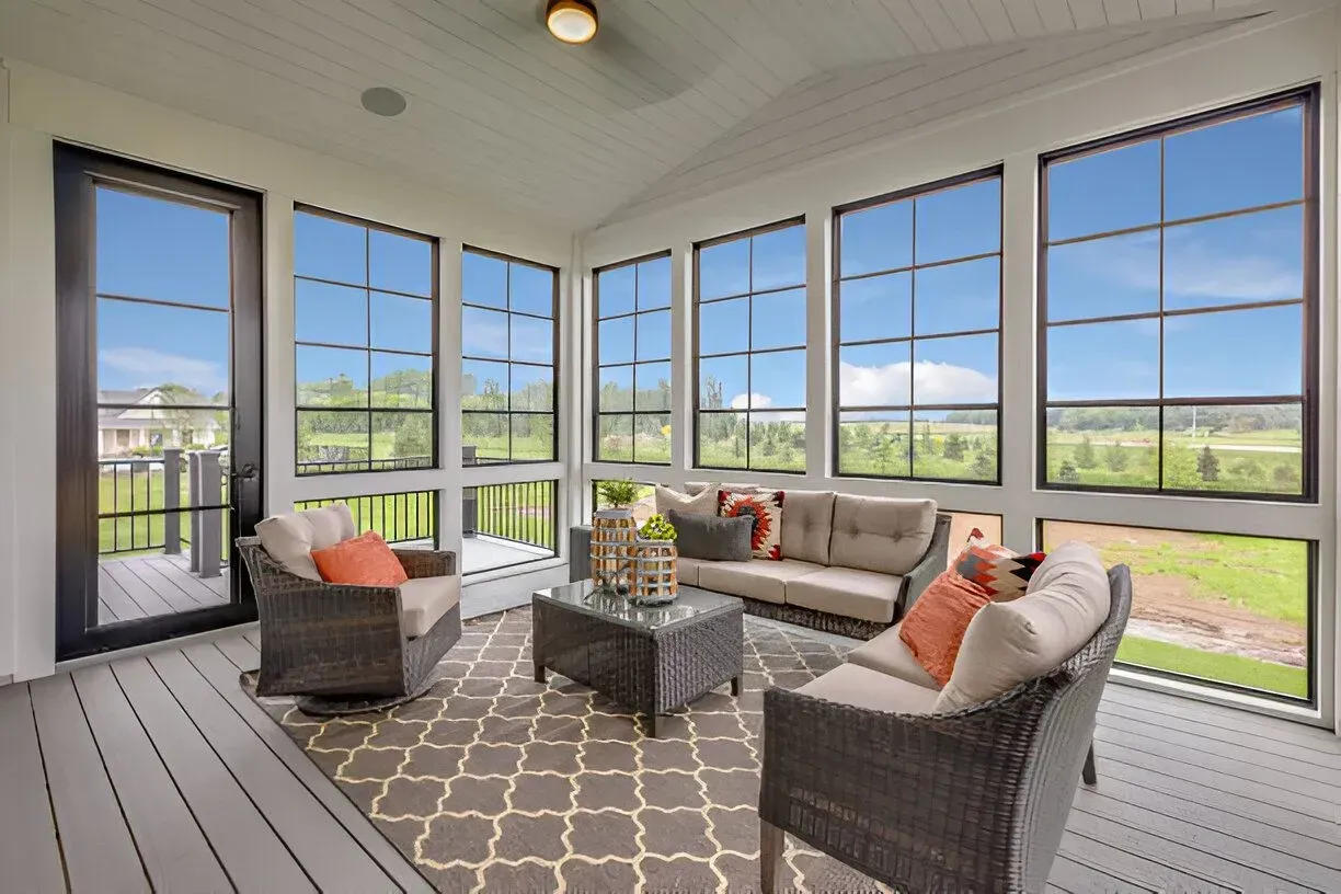 Sunroom with black-framed windows, wicker furniture, gray rug. 