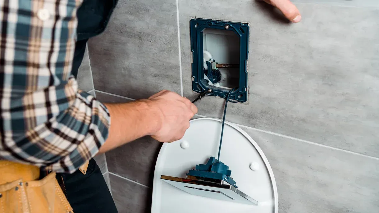 A man is fixing a toilet in a bathroom with a wrench.