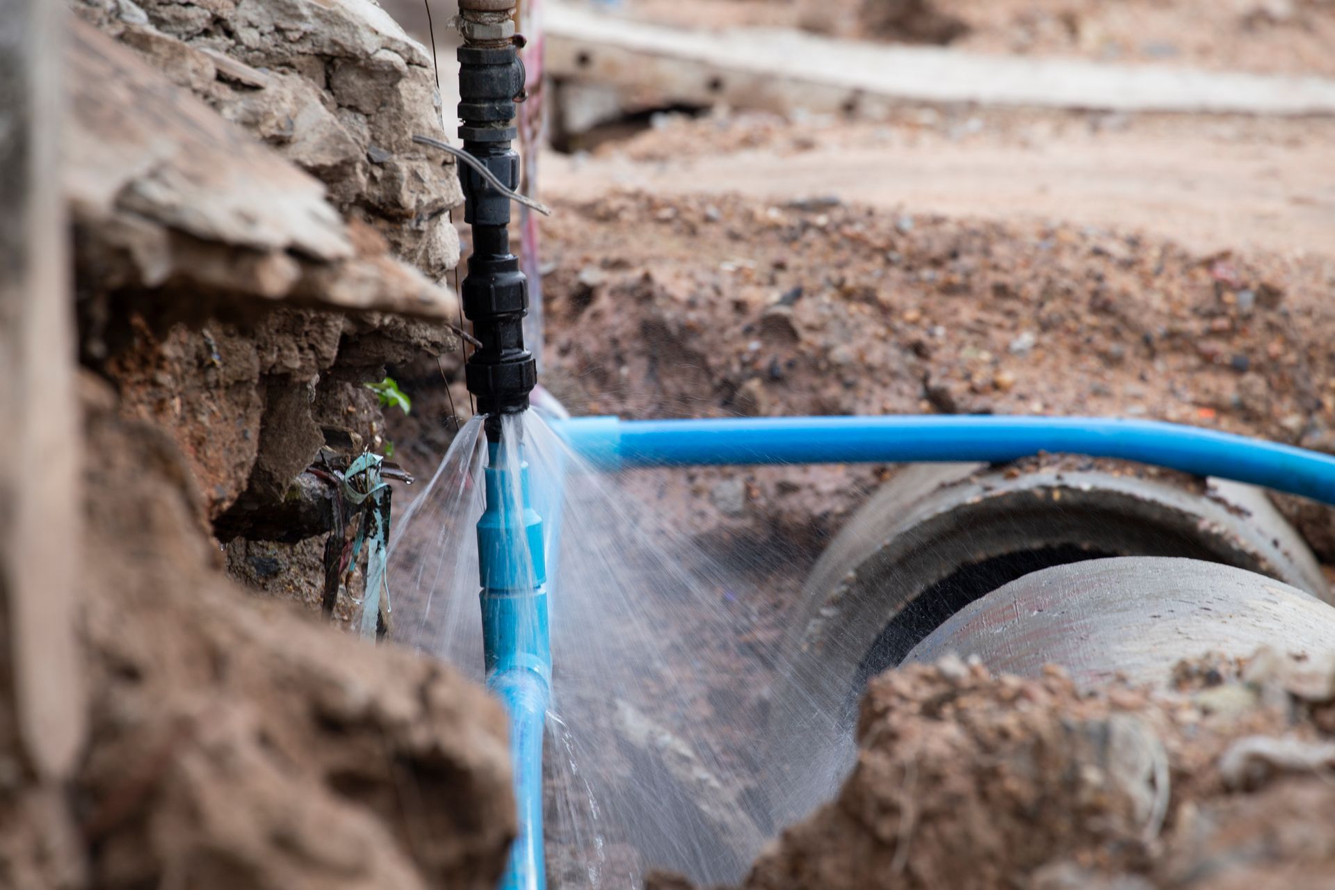 A blue pipe is leaking water into a concrete pipe.
