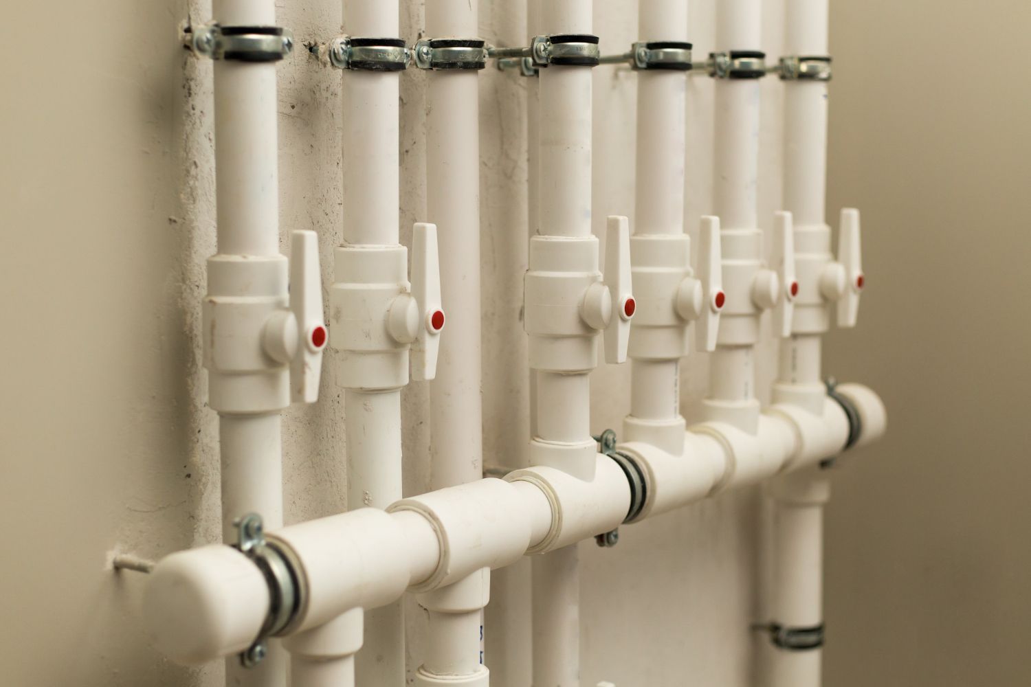 A row of white pipes with red valves attached to a wall.