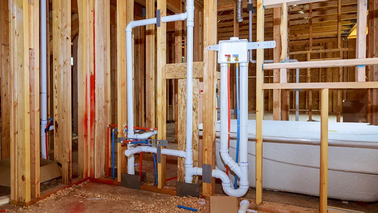 A bathroom in a house under construction with pipes coming out of the wall.