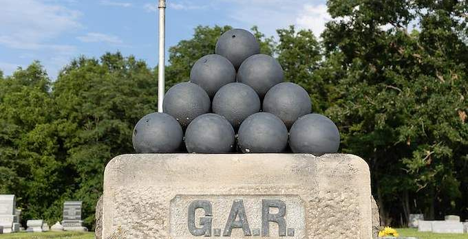 Stacked black cannonballs on a stone monument labeled G.A.R. outdoors under trees