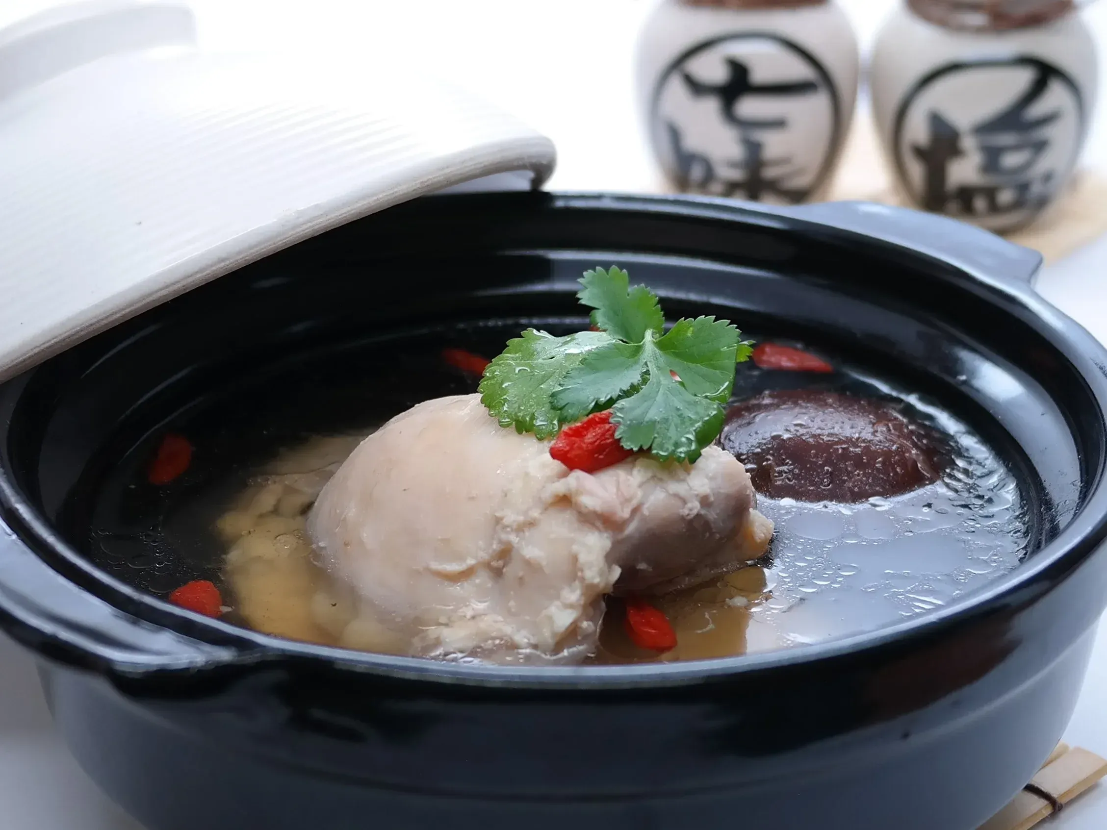 Steaming black bowl of braised meat in broth, garnished with cilantro and red chili peppers