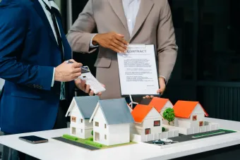 Two people reviewing a contract, with miniature houses on a table.