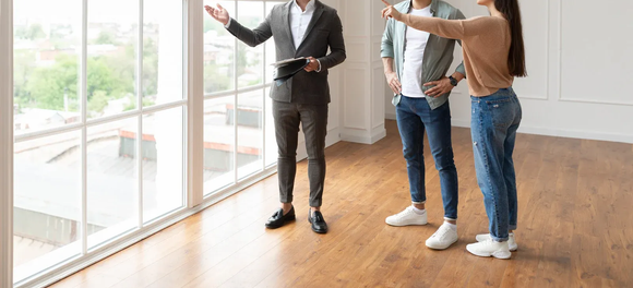 Real estate agent showing a couple a room with a large window, gesturing at the view.