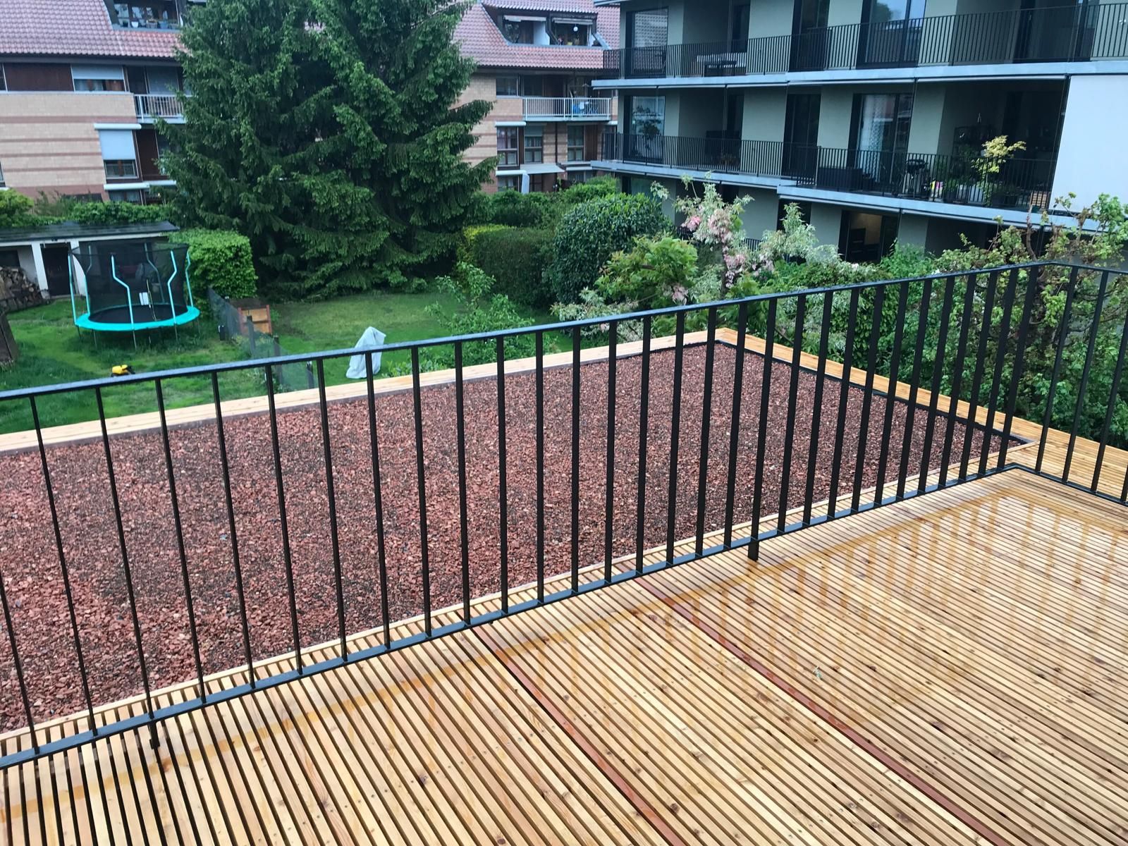 Eine Holzterrasse mit einem Metallgeländer an der Seite eines Gebäudes.