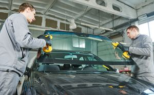 Two mechanics using tools on a black car in an auto repair garage