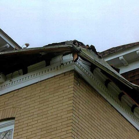 Damaged roof corner on a brick house with missing shingles and exposed structural damage