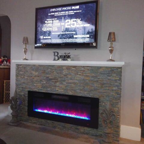 Living room fireplace with stacked stone surround, electric flame, and TV above displaying a promo ad