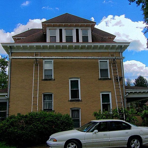 Brick house with white trim and a parked silver car in front under a blue sky