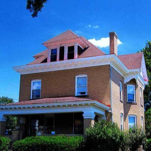 Brick two-story house with red roof, white trim, and a covered front porch under a blue sky
