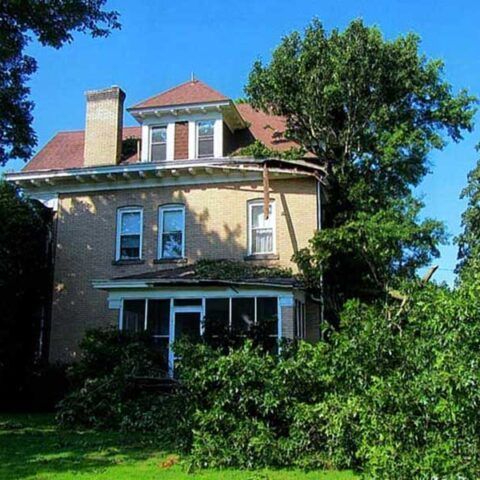 Three-story house with red roof and white trim, partly shaded by trees on a sunny day
