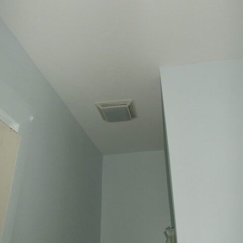 Ceiling corner with a white vent in a light gray room