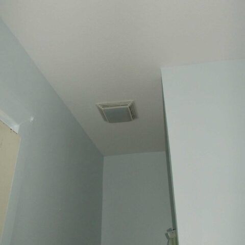 Corner of a room with a white ceiling vent and light gray walls