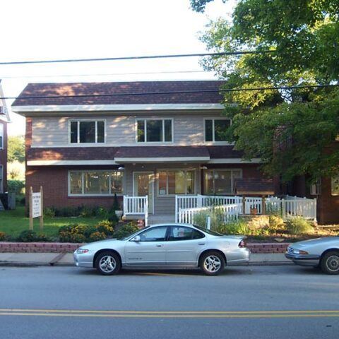Suburban two-story house with white fence and two parked cars in front