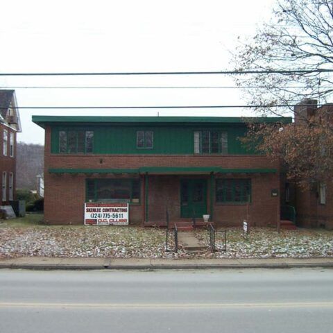 Brick and green two-story building with a vacant sign beside a road in winter