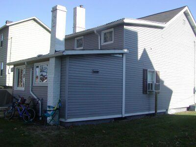 White two-story house exterior with gray siding, chimneys, and bicycles near the side porch