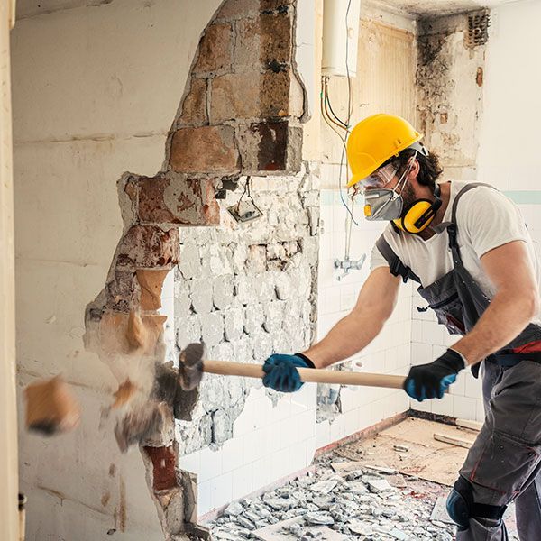 Construction worker in hard hat demolishing a brick wall with a sledgehammer inside a renovation site