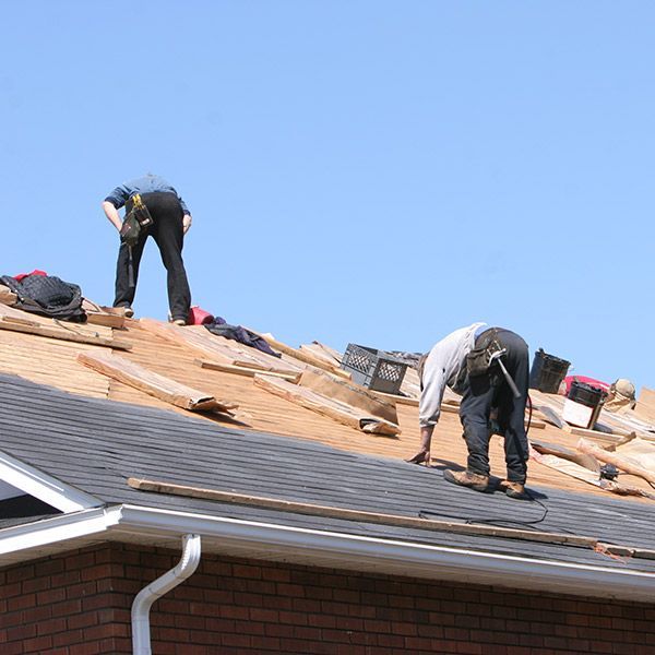 Roofers working on a house roof, laying underlayment and shingles under a clear blue sky.
