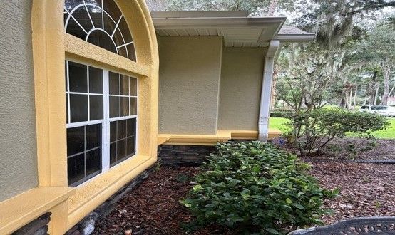 Yellow house exterior with arched window, beige wall, shrubs, and landscaped yard