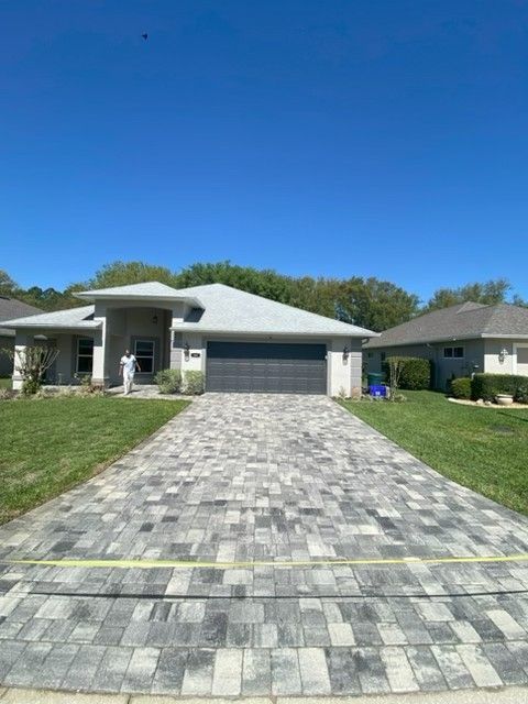 Single-story suburban house with a gray paver driveway and green lawn under a blue sky