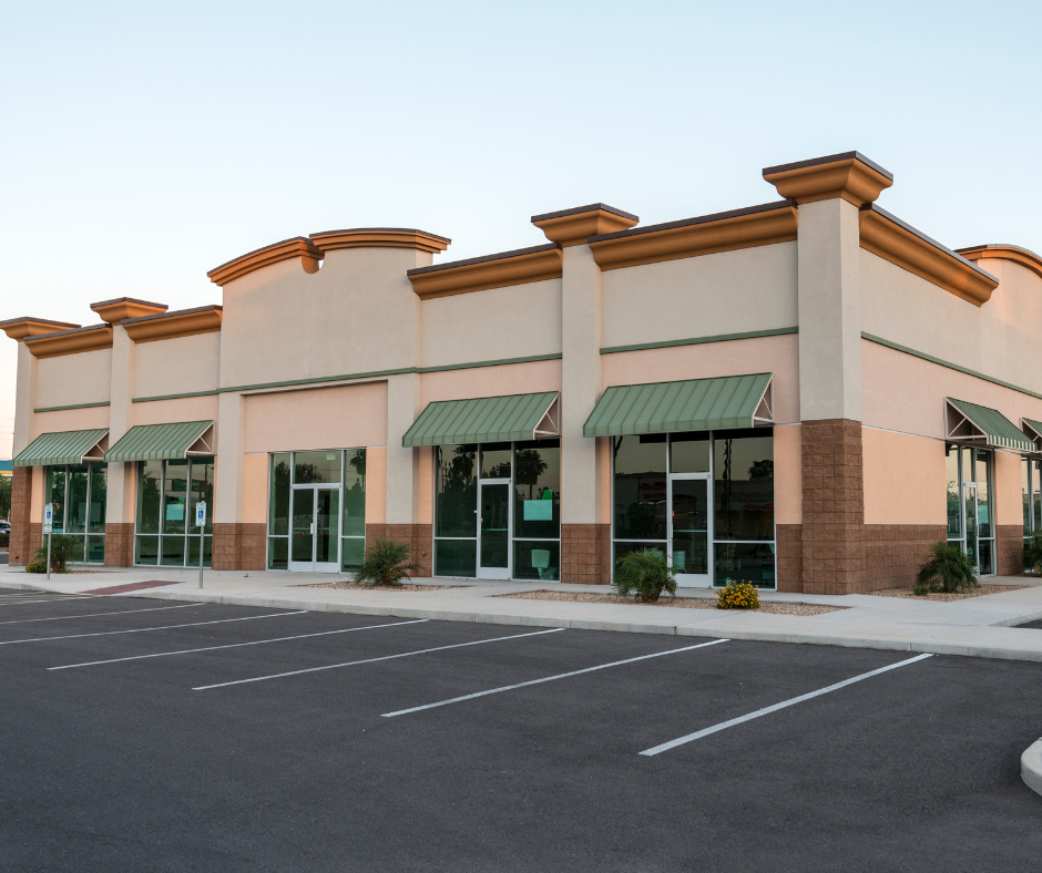 Empty commercial building with glass storefronts, parking lot in front.