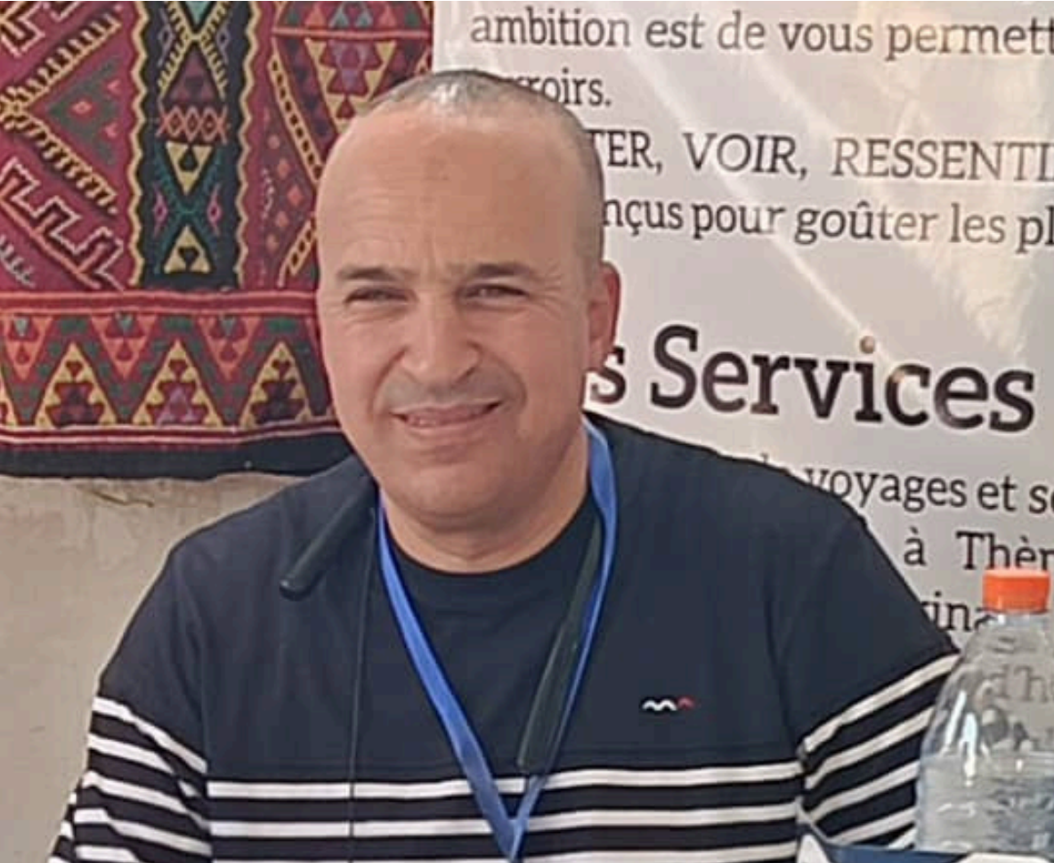 A person in a striped, long-sleeved shirt with a blue lanyard stands before a patterned textile and informational poster.