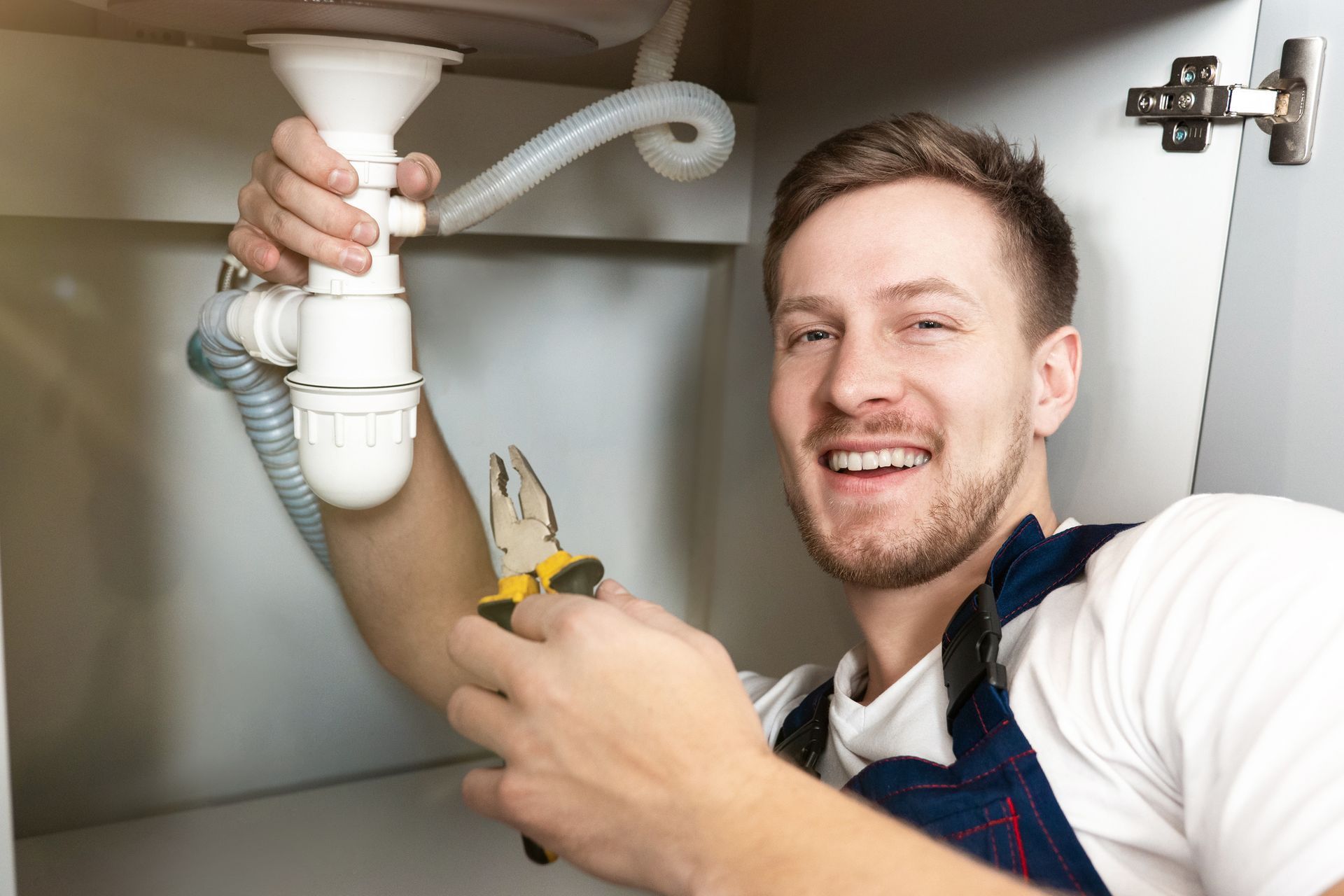 Smiling male plumber fixing the sink with pliers in his hand. Smiling male plumber fixing the sink with pliers in his hand.