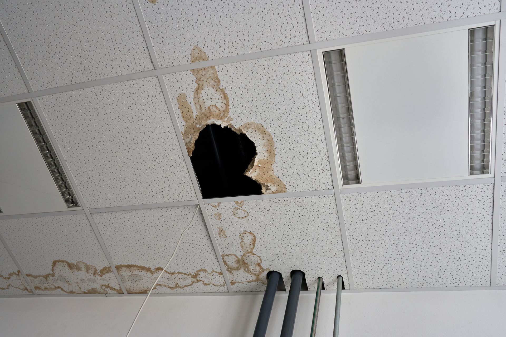 Water damage on a suspended office ceiling with a large hole and brown stains from a leak Water damage on a suspended office ceiling with a large hole and brown stains from a leak