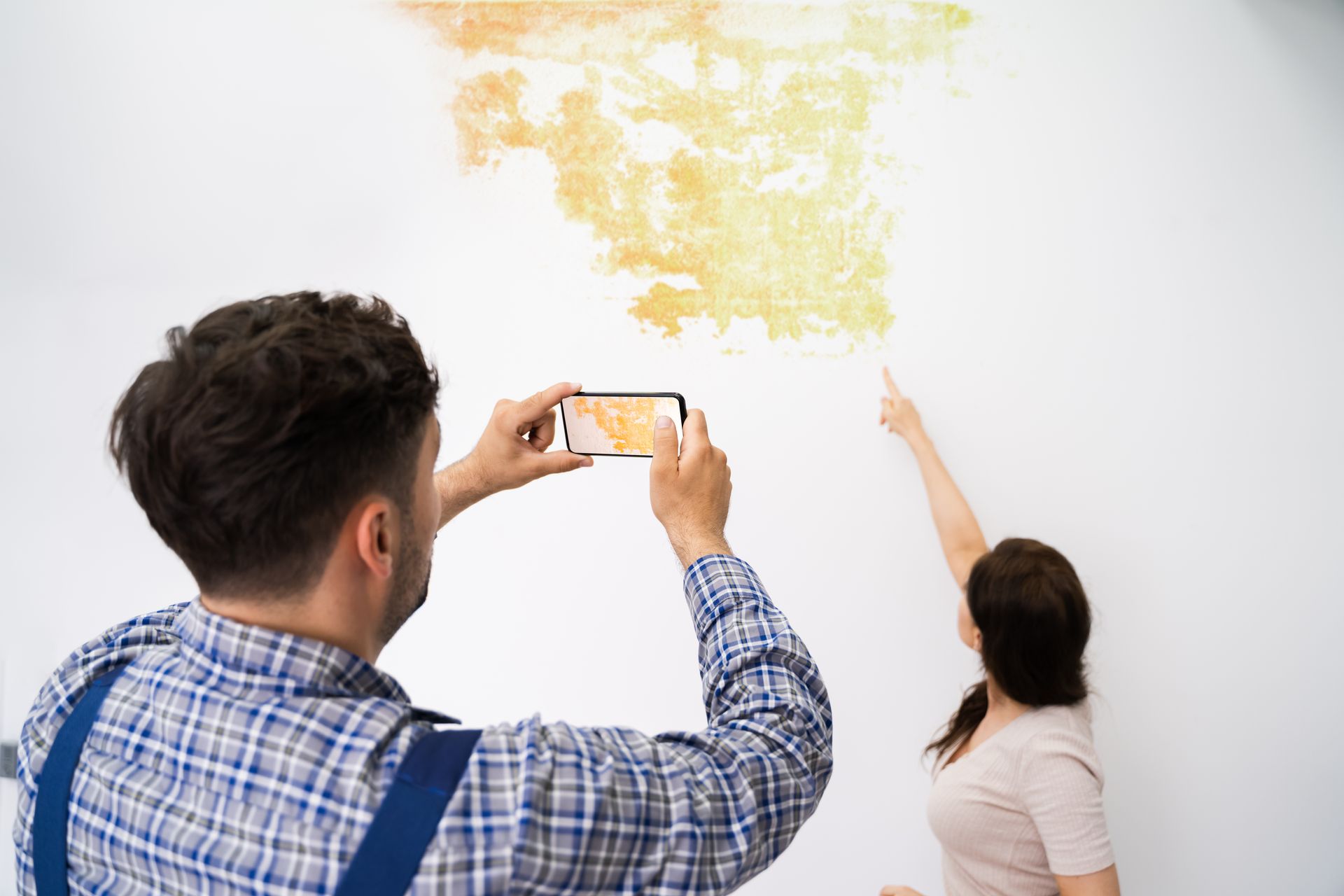 Person photographs mold damage on a wall while another points to affected area. Person photographs mold damage on a wall while another points to affected area.