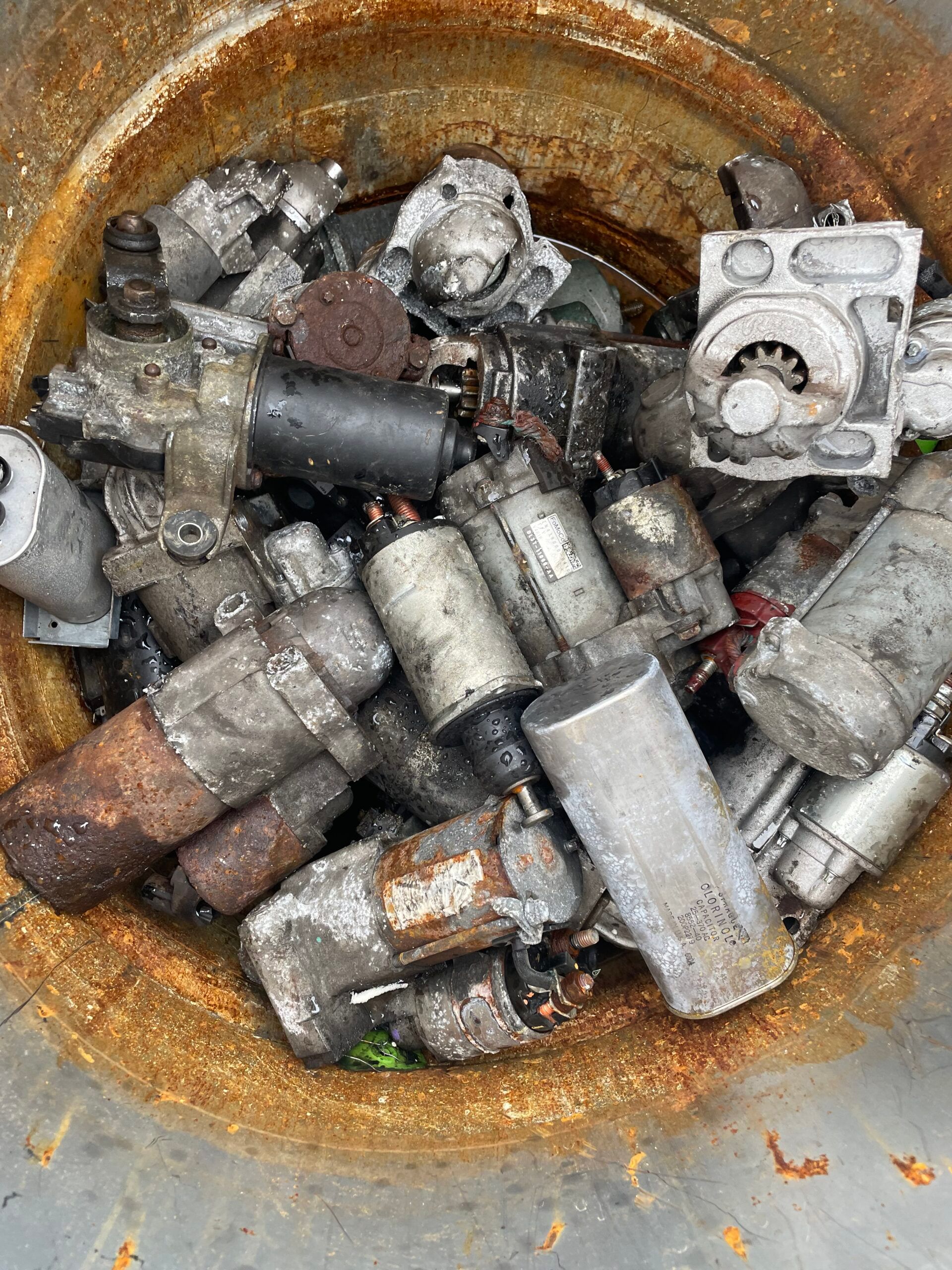 Rusty metal scraps and bolts piled in a round container, with a white component on top.