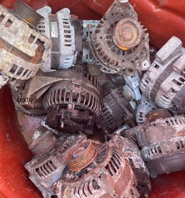 A pile of dusty, rusted metal alternators and engine parts in a red container.