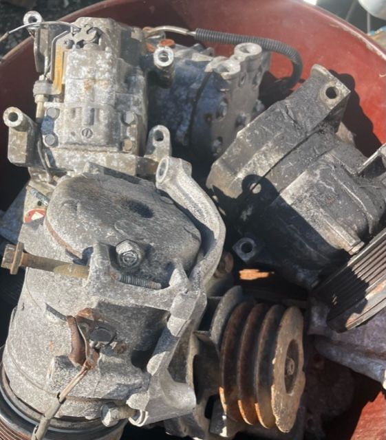 Pile of used car parts, including rusted metal components and a pulley, in a box.