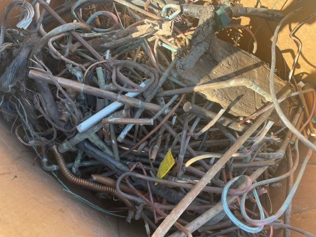 Pile of tangled metal scrap and bent rods in a junkyard, with rusted wires and pipes.